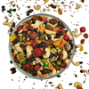 Nuts For Wellness Assorted trail mix in a glass bowl with scattered nuts and seeds on a white background