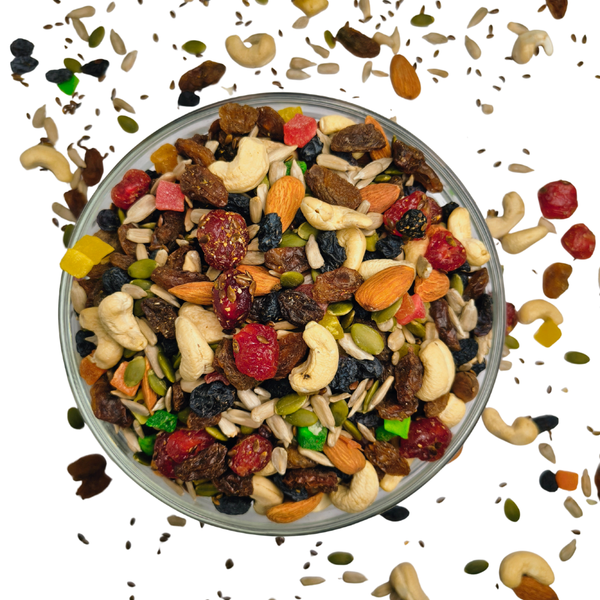 Nuts For Wellness Assorted trail mix in a glass bowl with scattered nuts and seeds on a white background