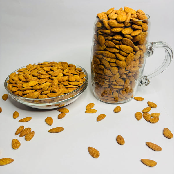 Glass bowl and mug filled with almonds on a white background
