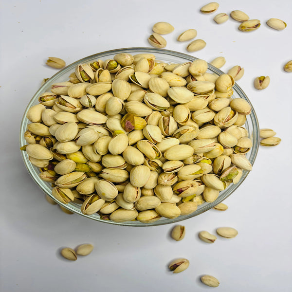 Glass bowl filled with pistachios on a light gray background