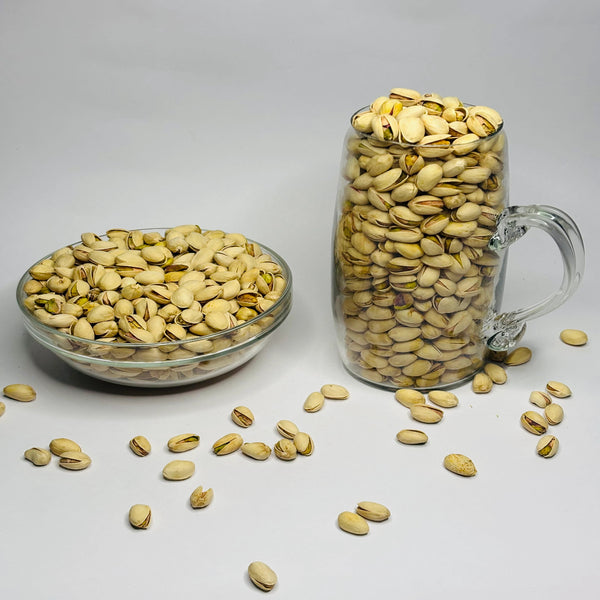 Glass bowl and mug filled with pistachios on a white background