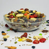 Glass bowl filled with a mix of dried fruits and nuts on a light gray background