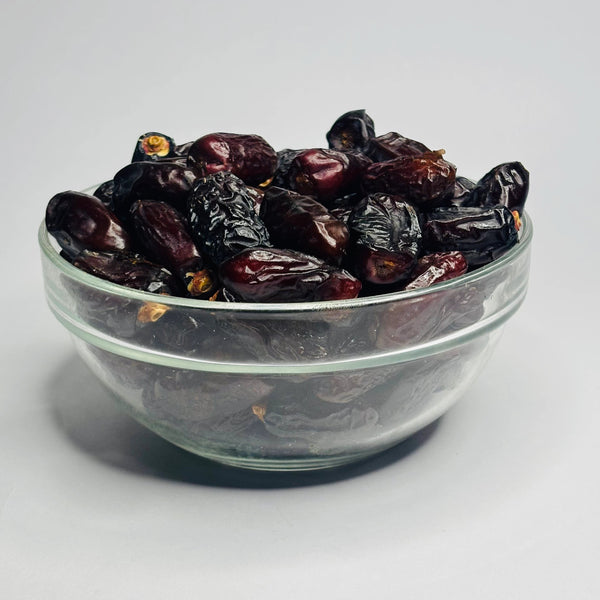 Glass bowl filled with dark dried fruits on a white background