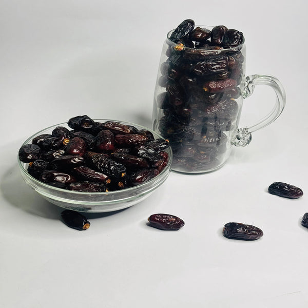 Glass bowl and mug filled with dark raisins on a white background