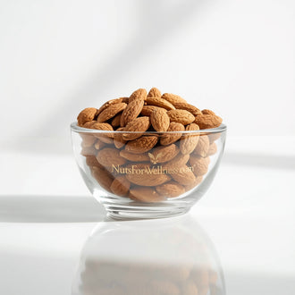 A clear glass bowl filled with Healthy Trail Mix from NutsForWellness sits on a white surface. Bright, natural light highlights the packaging’s gold lettering and casts soft shadows.