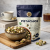 Nuts for Wellness Bag of premium pistachios 500g with a bowl of pistachios on a wooden board, next to a cup of coffee.