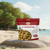 Nuts For Wellness Bag of premium cashews on a beach with trees and ocean in the background
