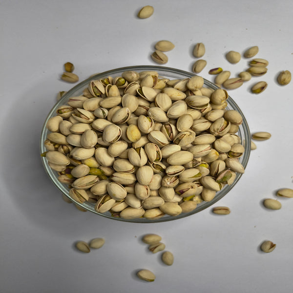 Glass bowl filled with pistachios on a light gray background