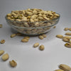 Glass bowl filled with pistachios on a light gray background