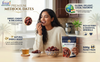 A woman in a cream knit sweater is shown eating a medjool date while holding a bag of Fssai Premium Medjool Dates. The scene is set in a warm kitchen environment with various text overlays highlighting the product's benefits, such as 'Sweet, Chewy & Delicious' and 'Natural Energy Boost'.