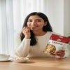Woman eating cashew nuts from a package with a bowl of cashews on a table.