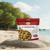 Bag of premium cashews on a beach with trees and ocean in the background