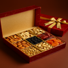 Open red gift box with a gold bow containing various dried fruits and nuts on a brown background.